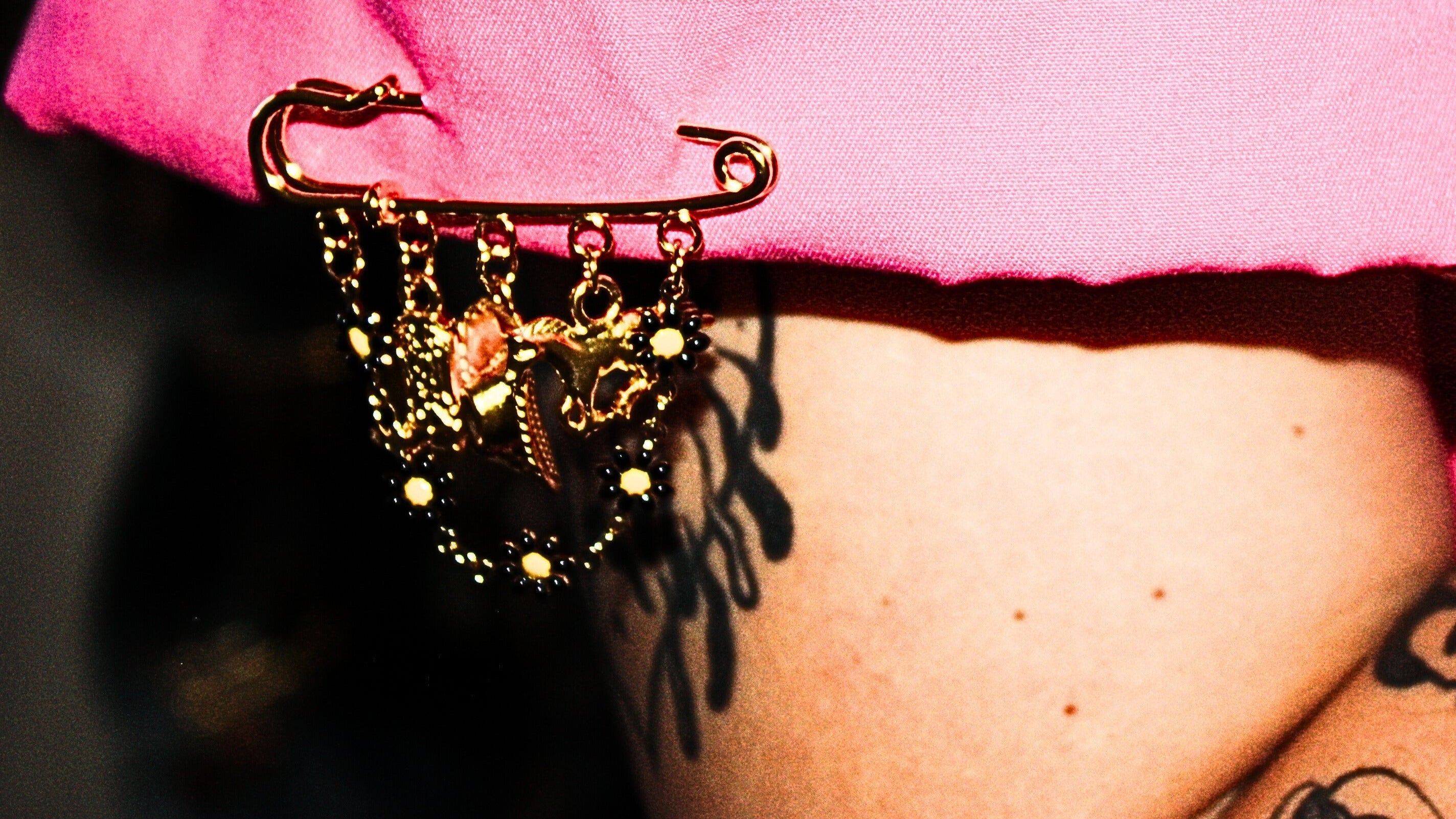Person wearing a pink shirt with a decorative black and gold brooch on a blurred background
